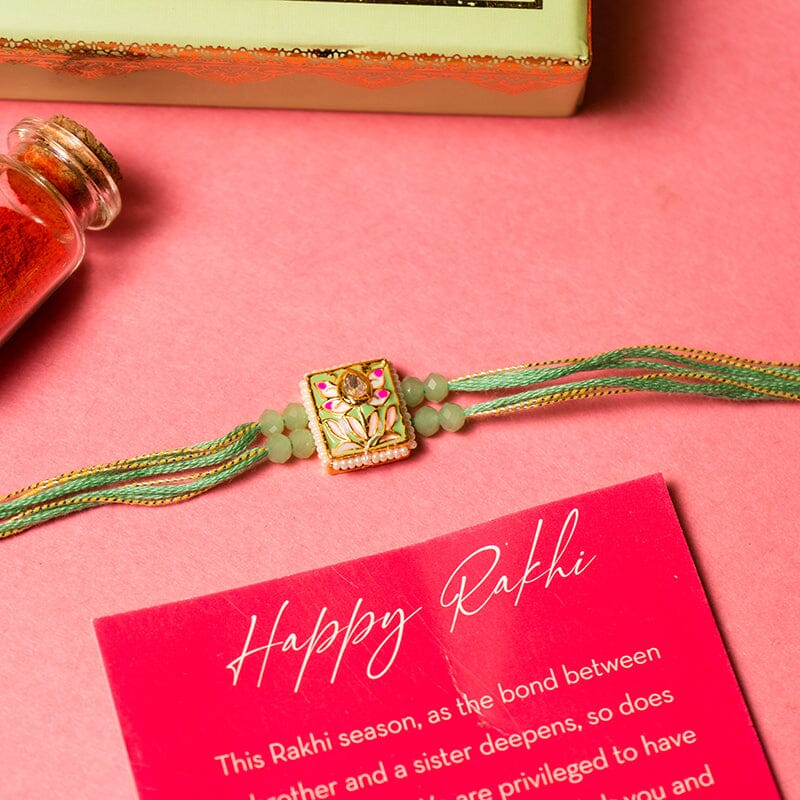 A Rakhi with green color threads and beads and a metal piece with flower on it.
